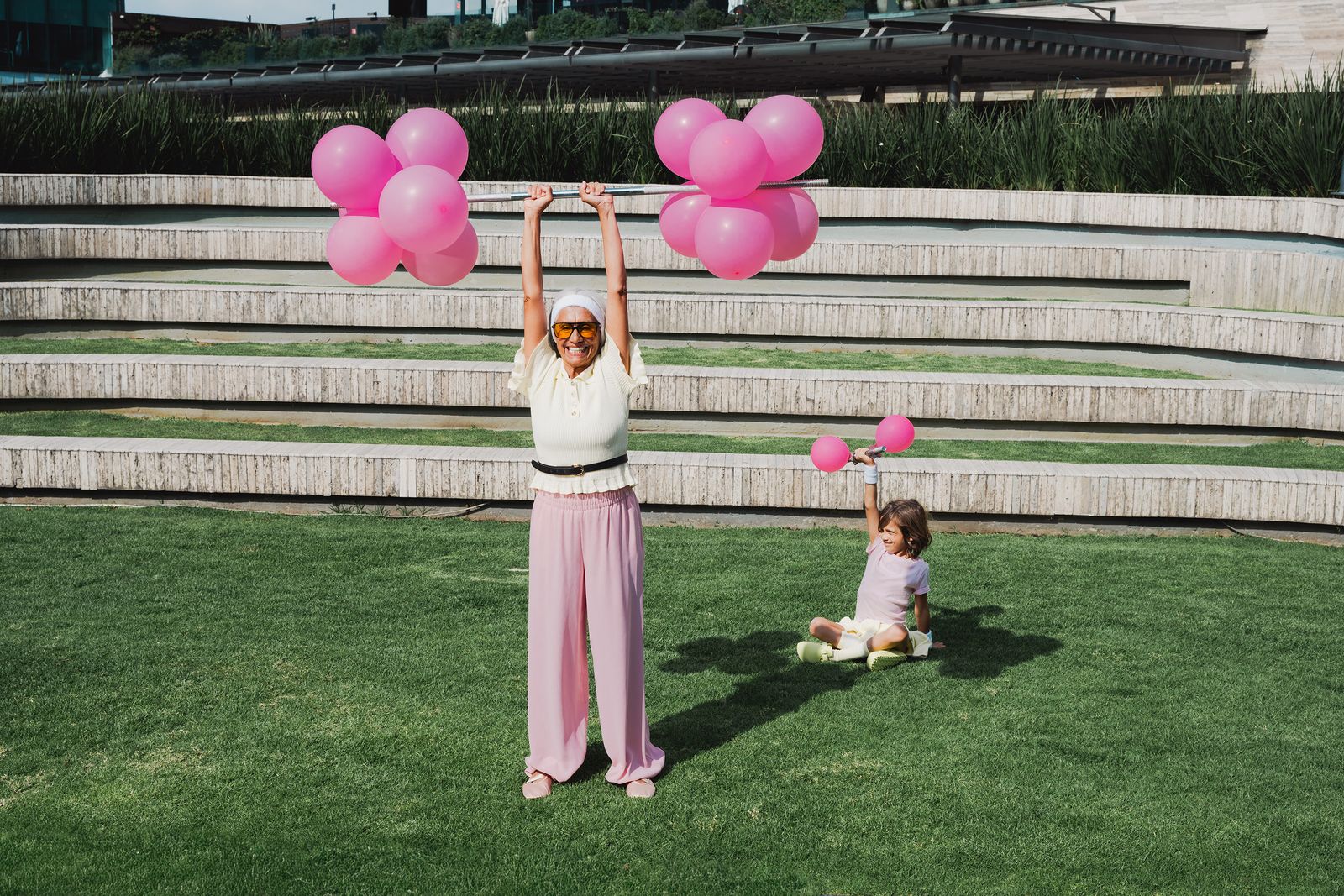 mujer mayor y niña jugando con globos rosas en jardín